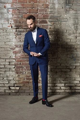 Homme en costume bleu marine sur mesure contre un mur de briques
