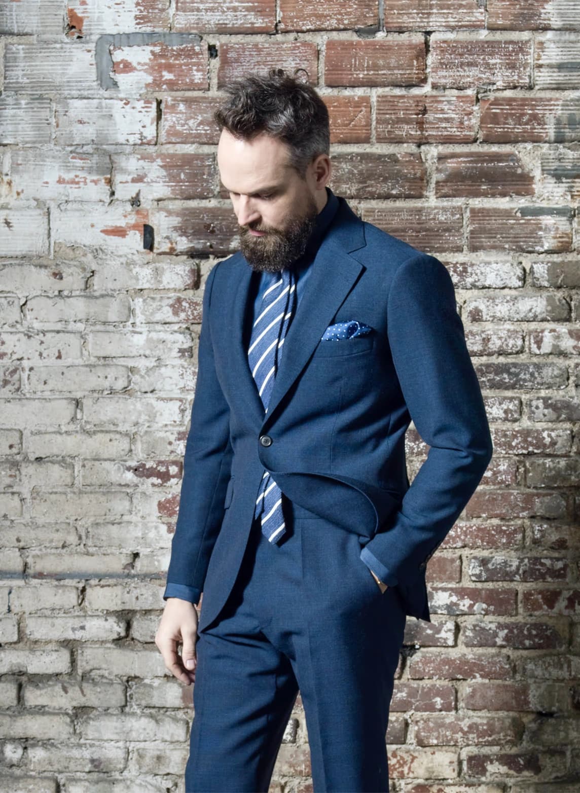 Homme en costume bleu navy avec cravate rayée contre un mur de briques